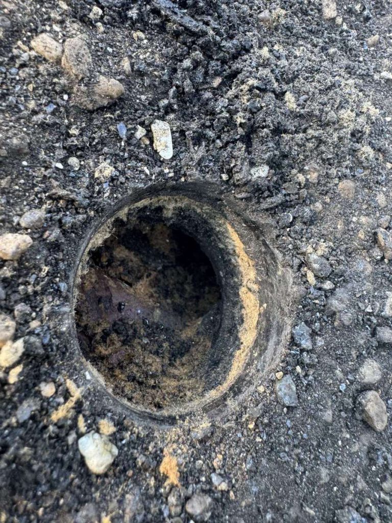 A badly corroded roof drain collar surrounded by loose gravel on a flat roof