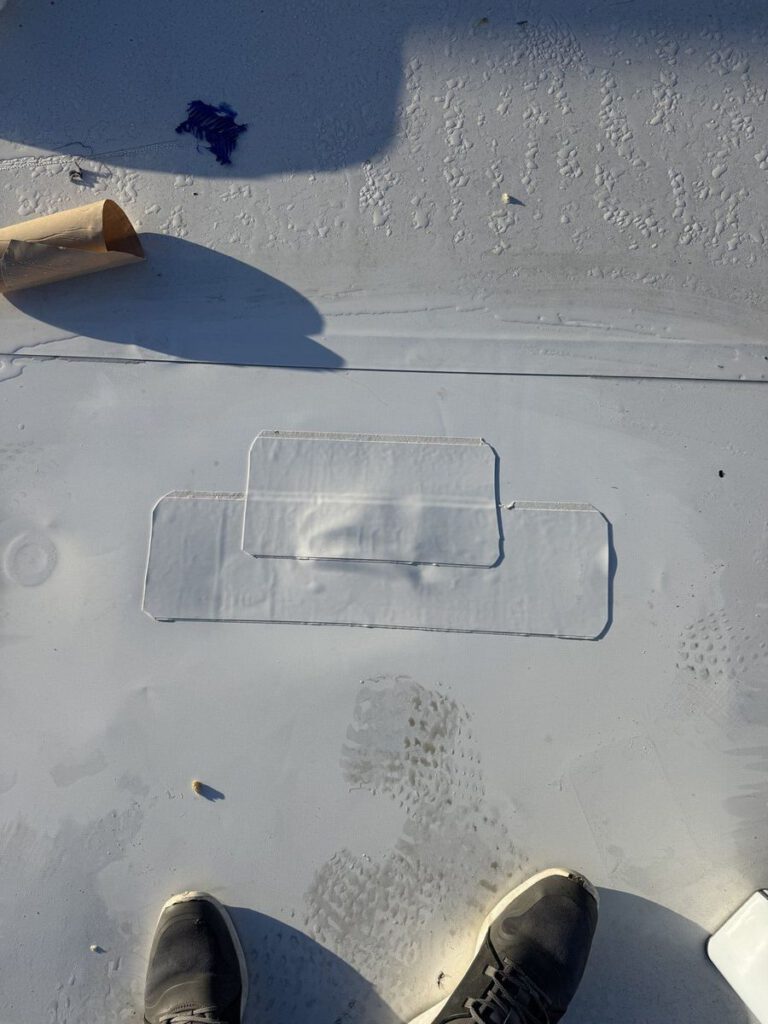 Two freshly welded patches sealing a repaired section of white flat roof membrane