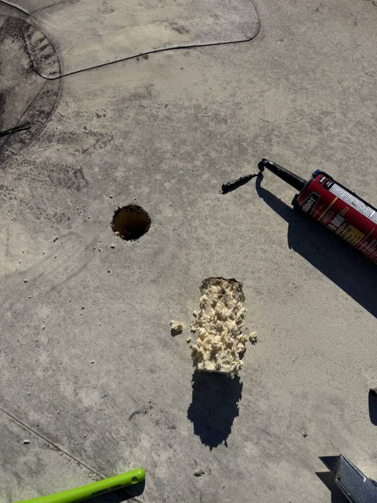 A core cut through a grey flat roof with the foam sample lying beside it and a tube of roof repair sealant in frame