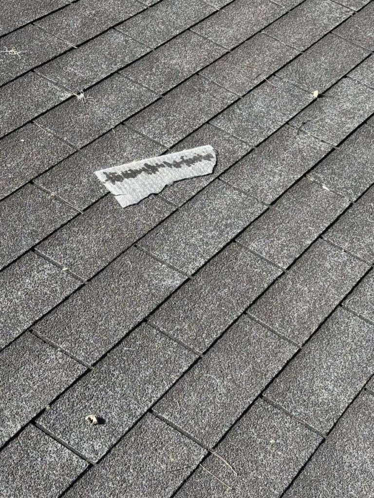 A torn-off piece of asphalt shingle lying loose on a shingle roof